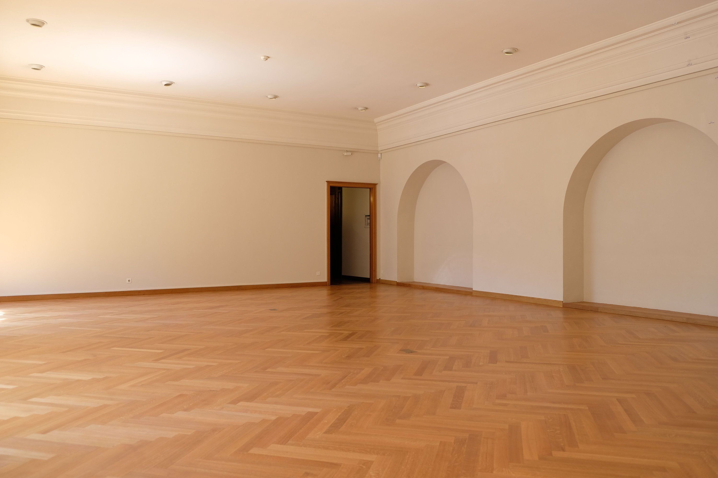 Leerer, frisch renovierter Altbausaal mit Stuckgesims, Rundbogennischen, weißen Wänden und Fischgrät-Parkett