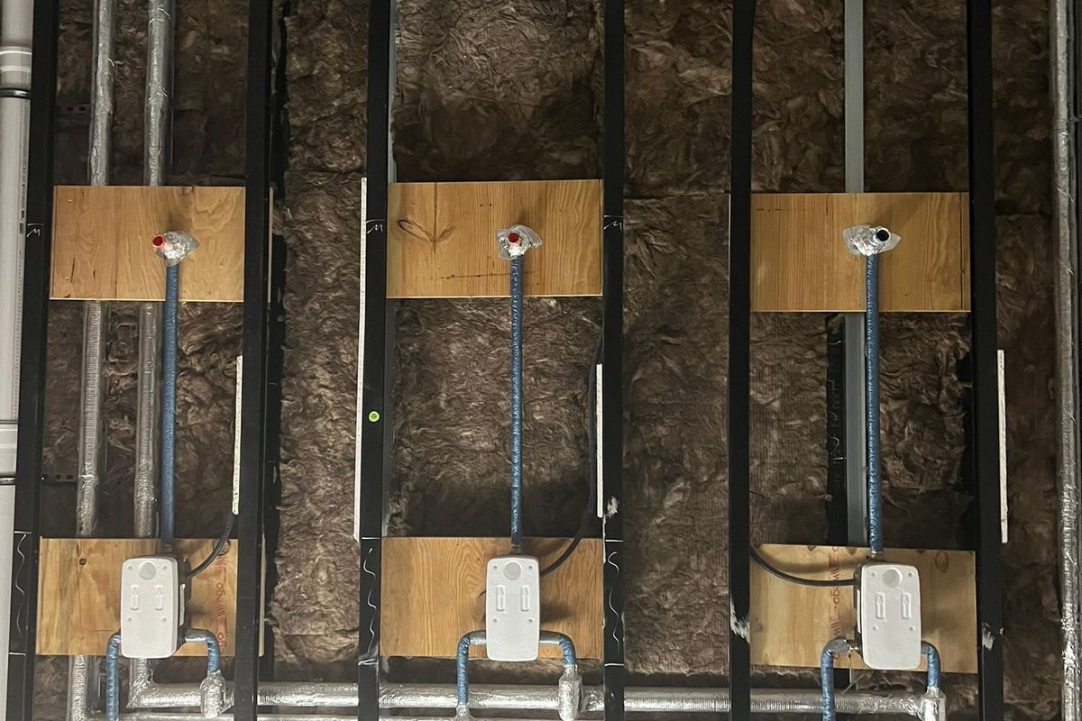 Freigelegte Installationswand mit drei Wasseranschlüssen, Dämmwolle und Lüftungsrohren
