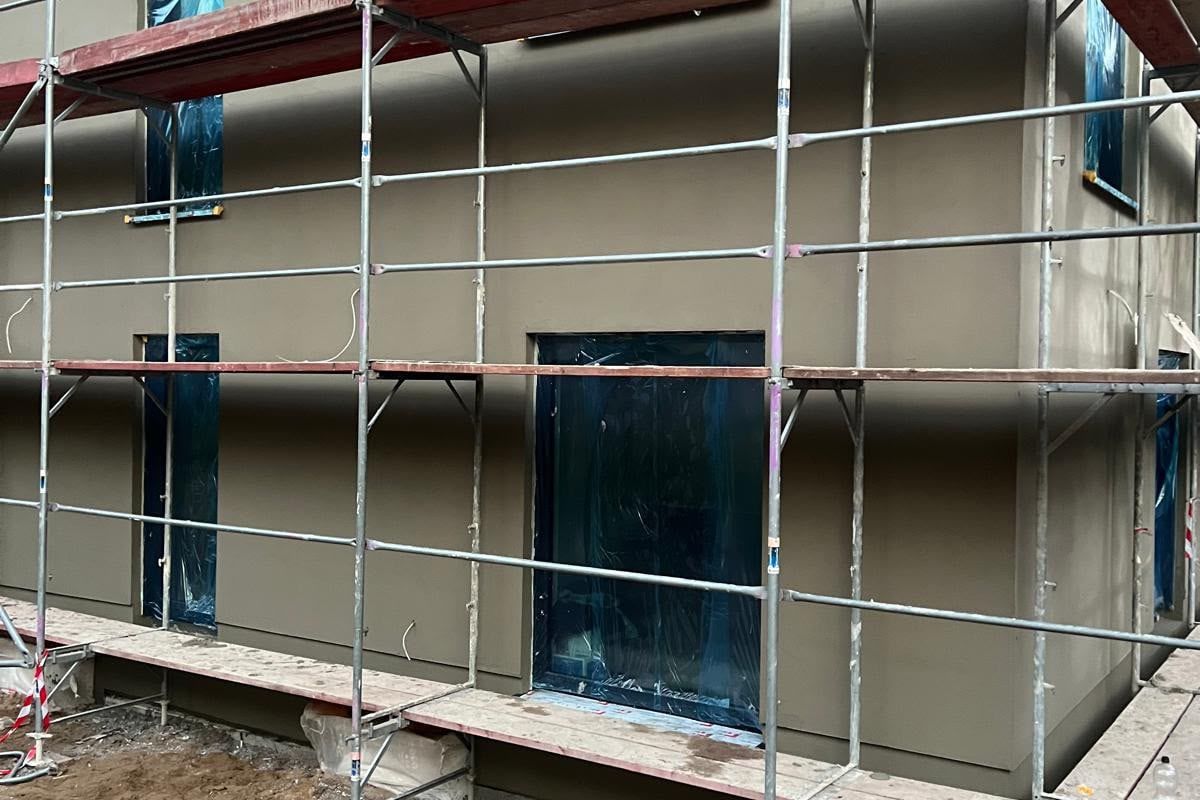 Eingerüstete Fassade eines Neubaus mit Grundputz und abgeklebten Fenstern