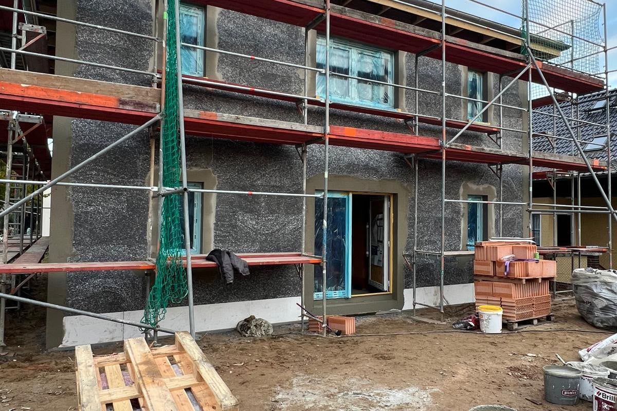 Rohbau mit Gerüst, Dämmputz an der Fassade und Ziegelpaletten auf der Baustelle