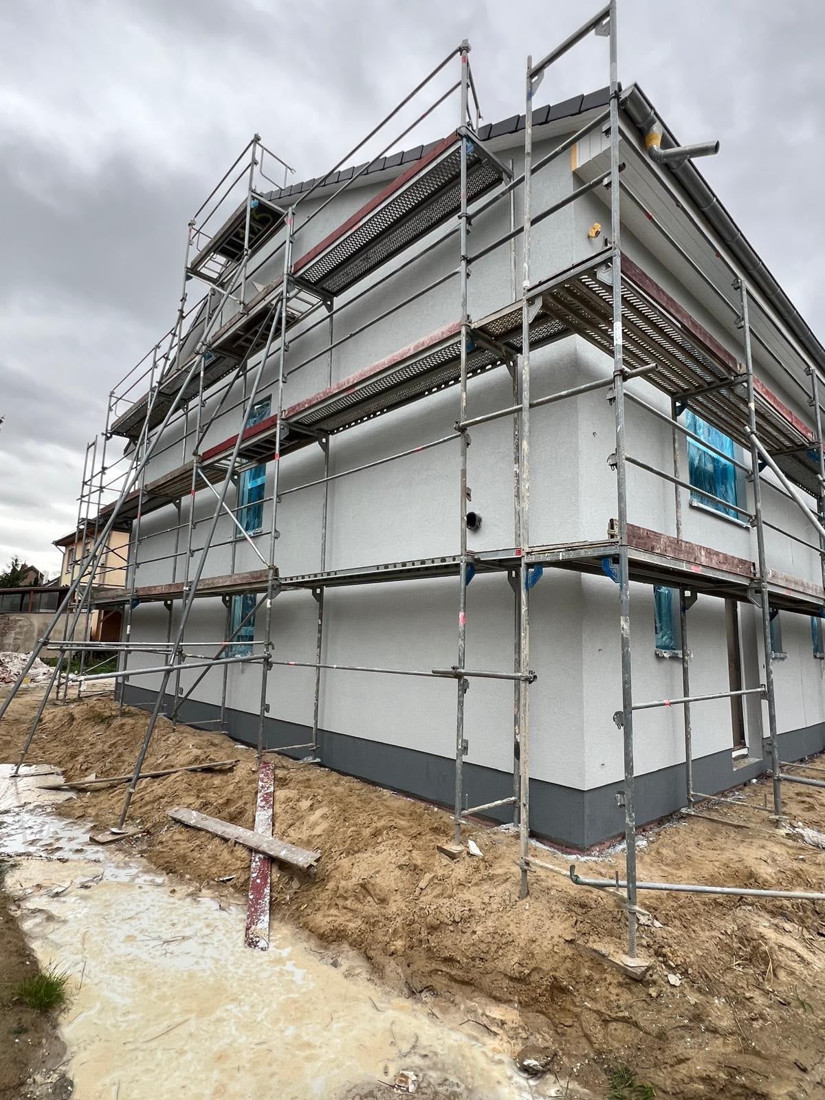 Eingerüsteter Neubau mit fertig verputzter Fassade und grauem Sockel