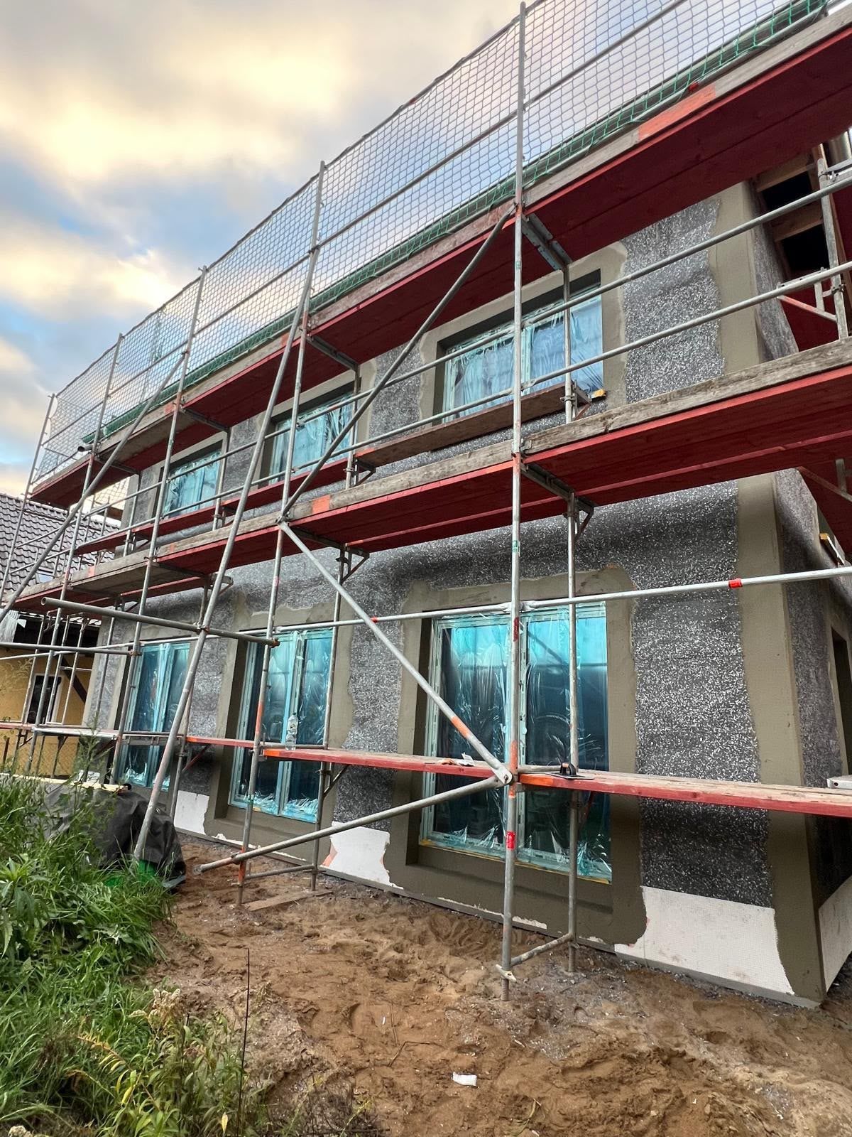Eingerüstete Neubaufassade mit Dämmputz und abgeklebten Fenstern