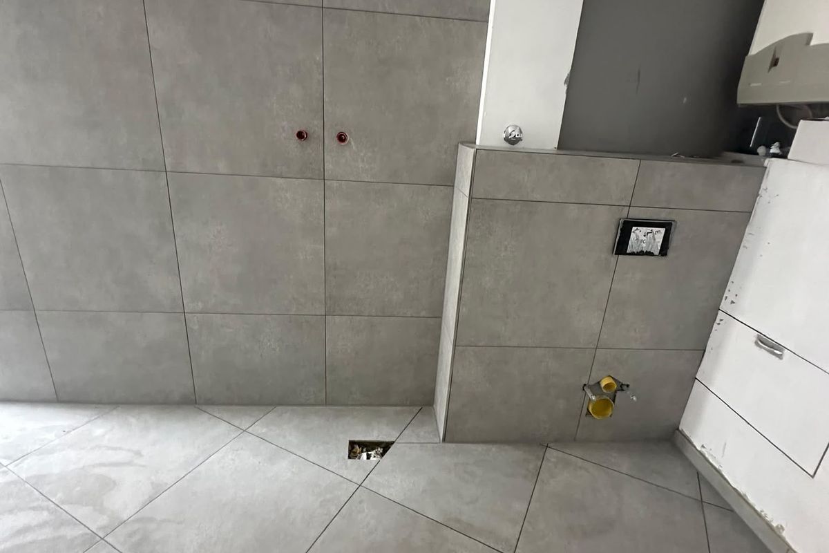 Bad mit grauen Großformatfliesen an Wand und Boden und gefliester Vorwand für das wandhängende WC