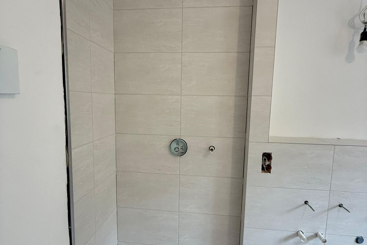 Geflieste Dusche mit hellen Wandfliesen, Duschrinne und vorbereiteten Armaturanschlüssen