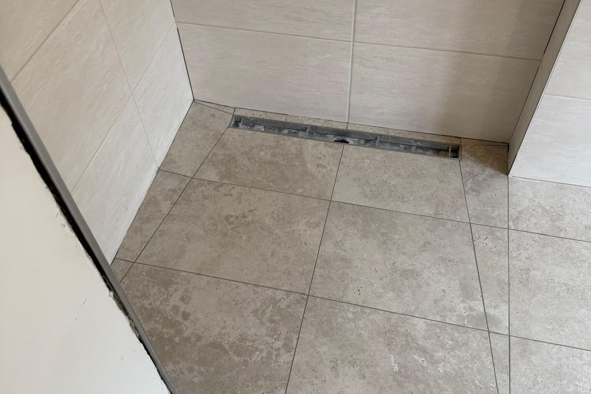 Bodengleiche Dusche mit hellen Wandfliesen, großformatigen Bodenfliesen und Duschrinne