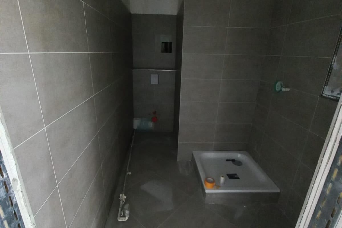 Bad mit grauen Wand- und Bodenfliesen, Duschtasse und Vorwand für das WC