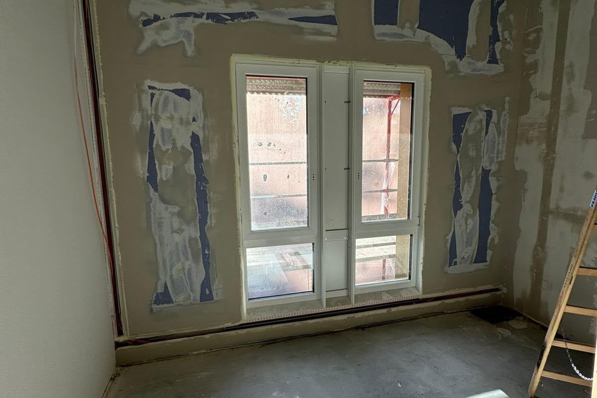 Raum in der Sanierung mit gespachtelten Wänden, neuer Fenstertür und Betondecke