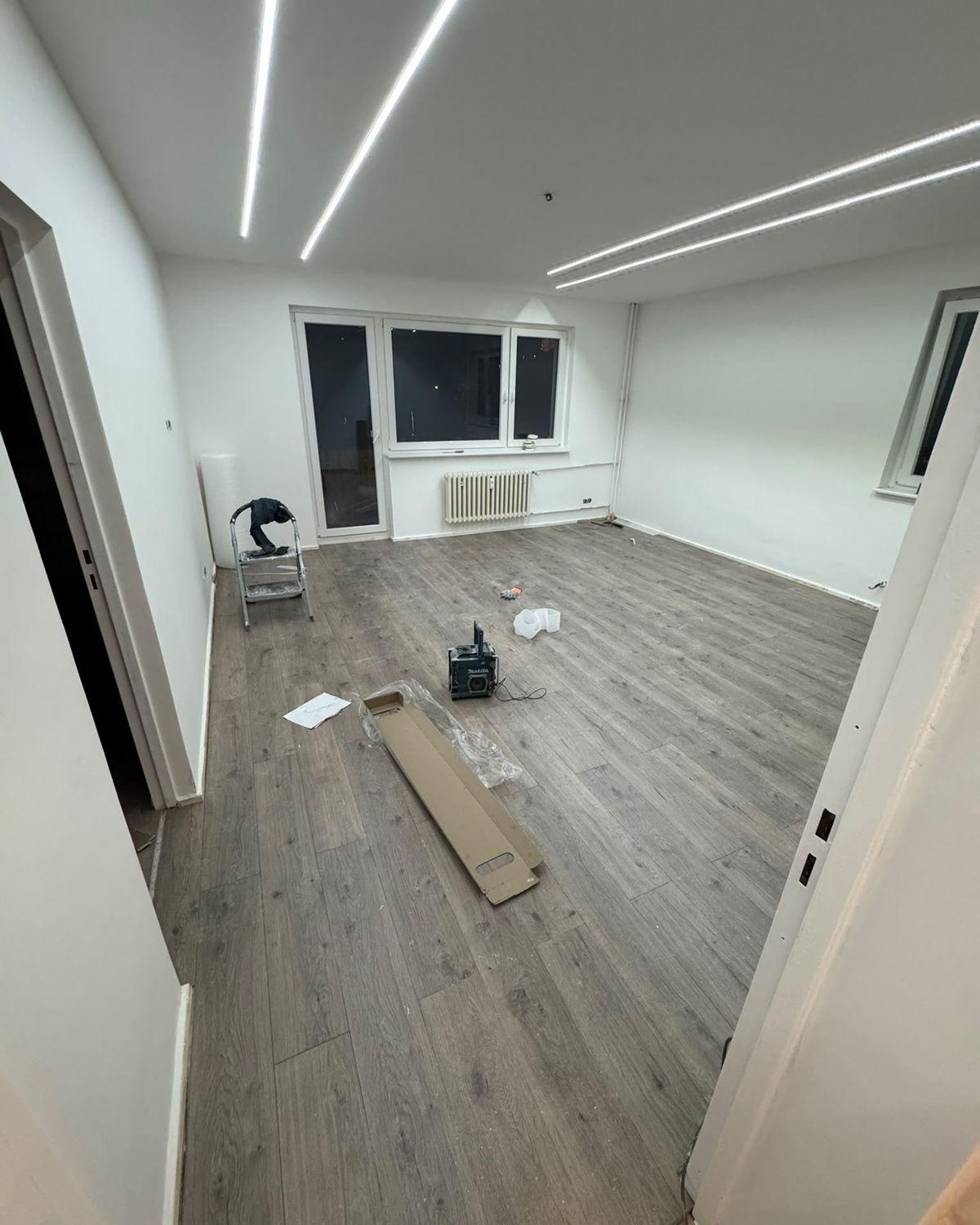 Renovierter Raum mit neuem Boden in Holzoptik, weißen Wänden und Lichtlinien an der Decke