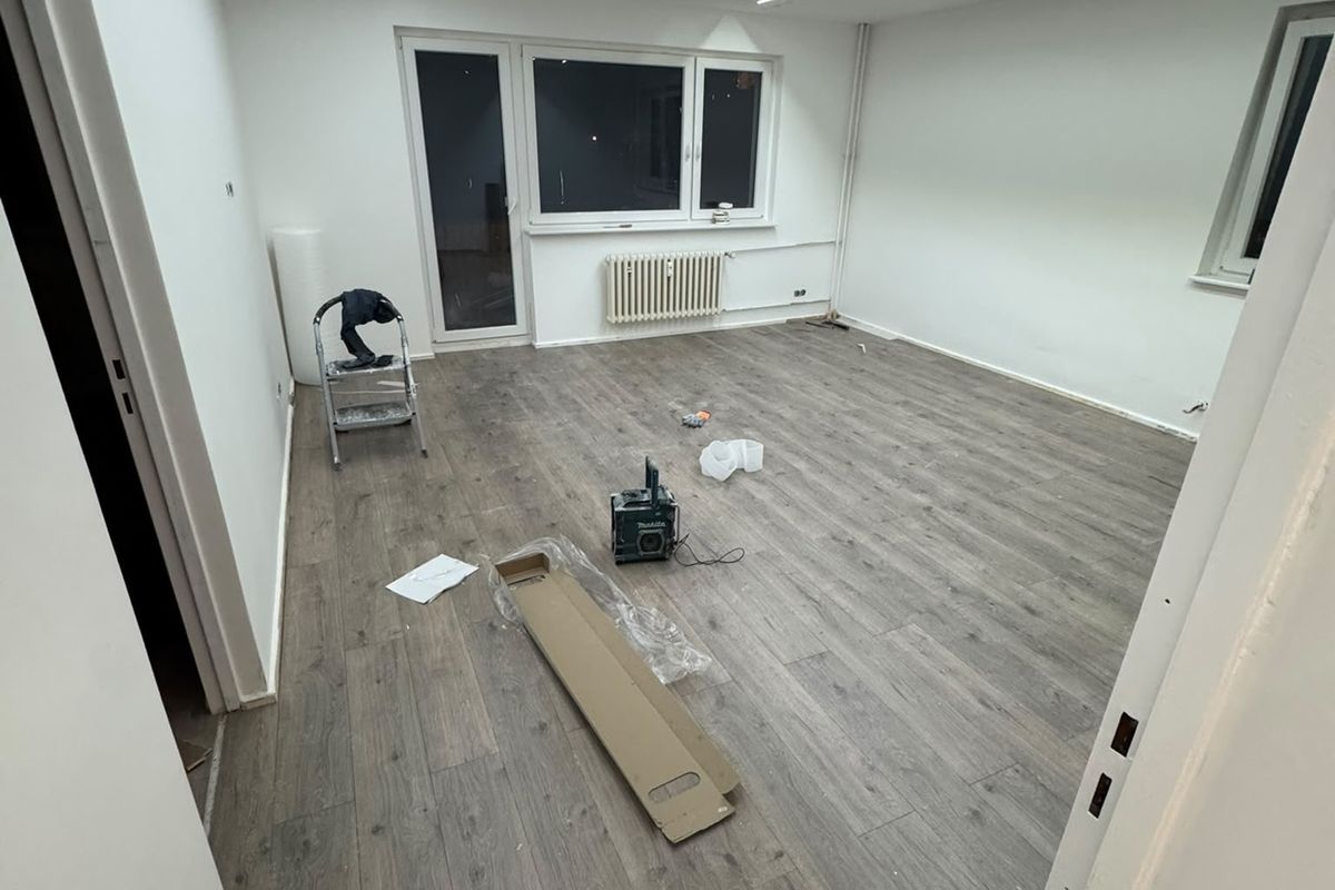 Renovierter Raum mit neuem Boden in Holzoptik, weißen Wänden und Lichtlinien an der Decke
